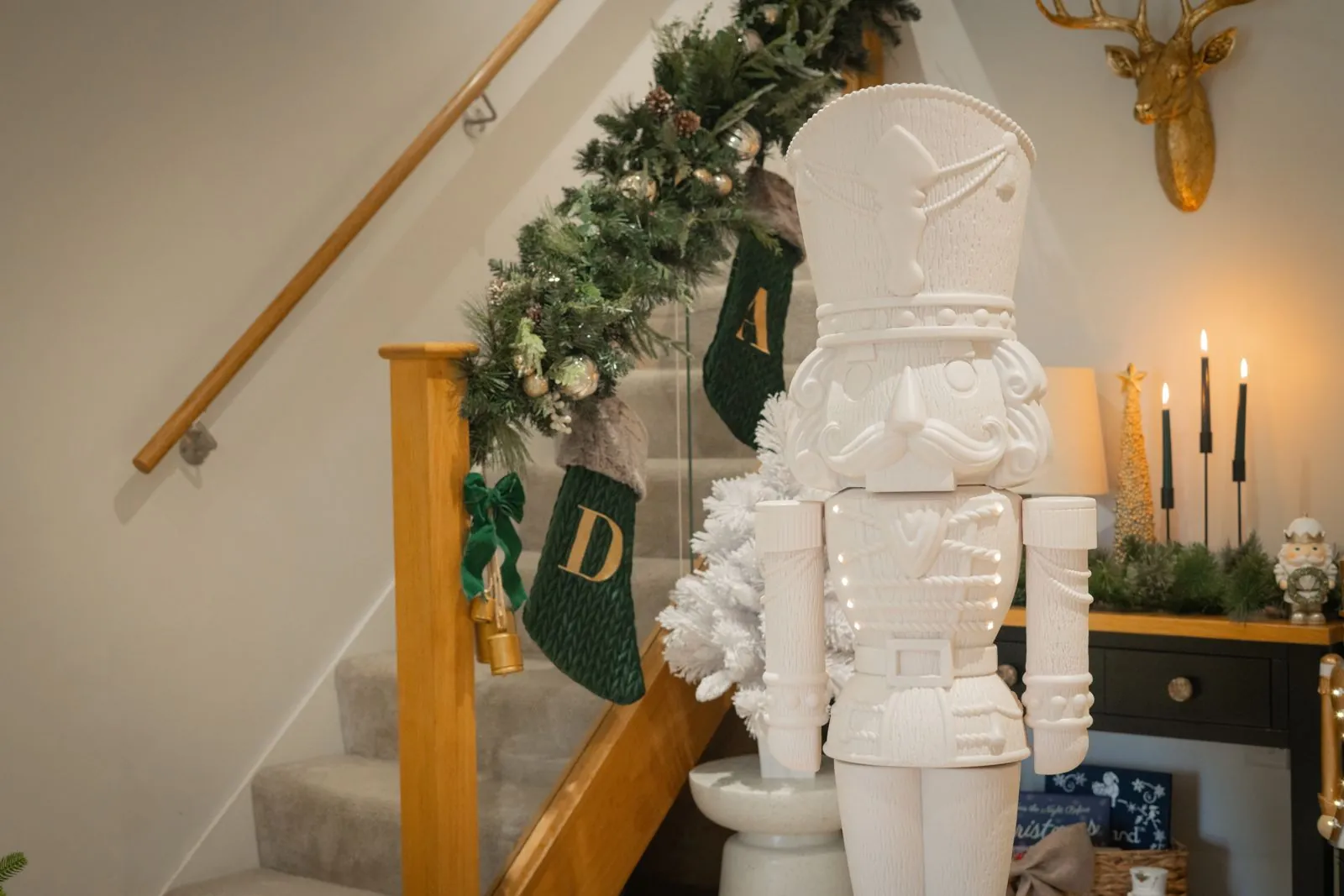 Plain white Paint Your Own Otto nutcracker at the foot of a staircase dressed with garland and stockings